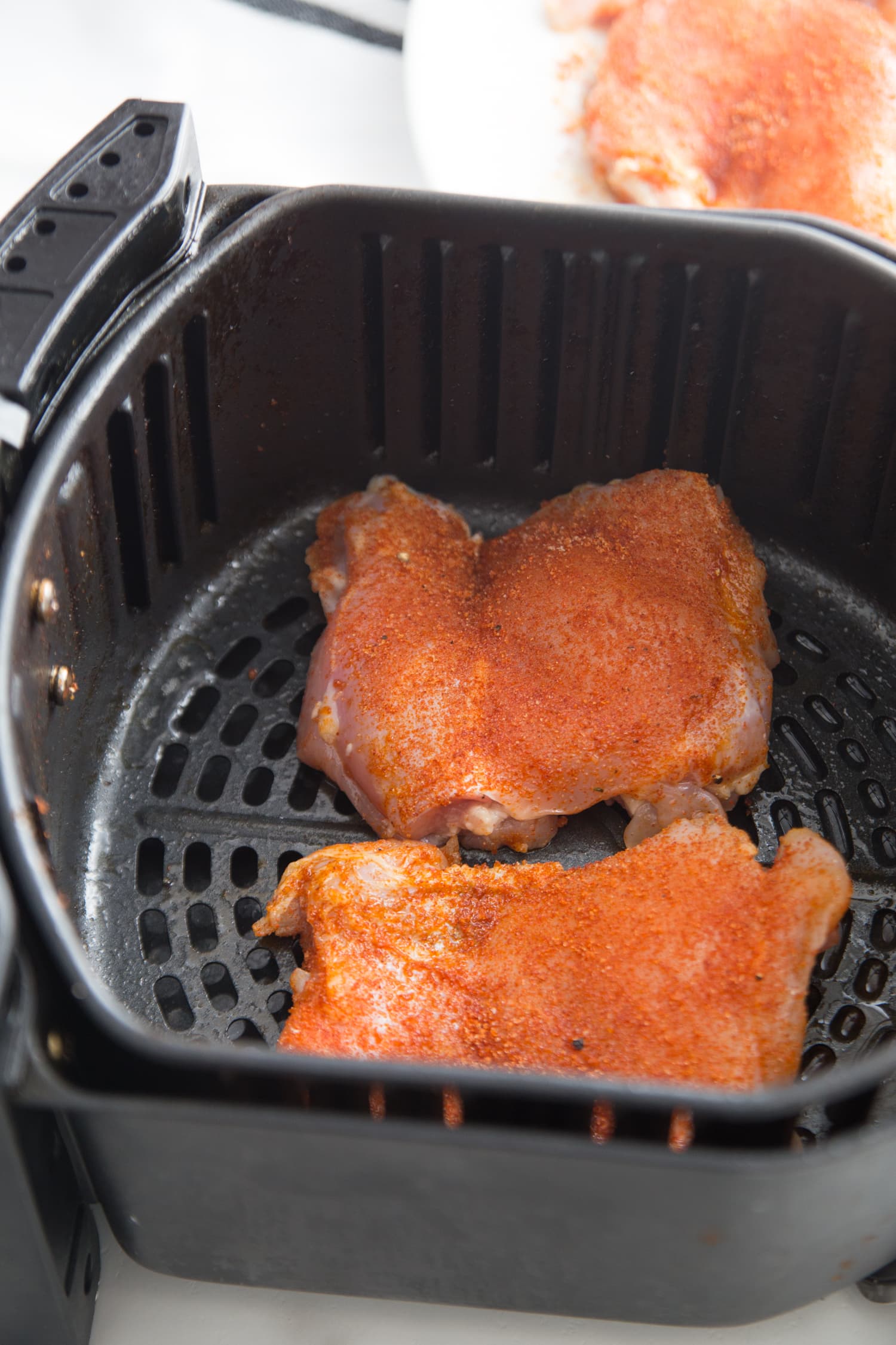 Seasoned chicken thighs in an air fryer basket.