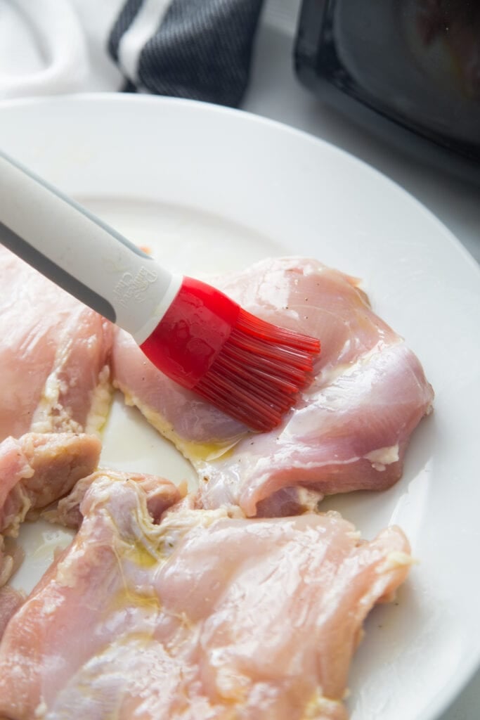 brushing olive oil onto pieces of boneless skinless raw poultry