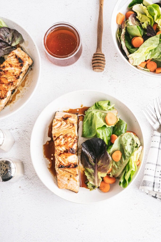 overhead photo of plated grilled salmon dinner on white background with salad, jar of honey and dipping wand