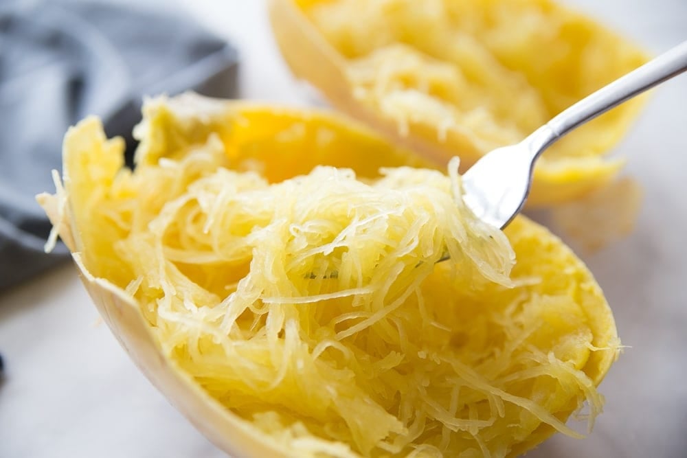 Cooked spaghetti squash half with squash strands on a fork, ready for a bite.