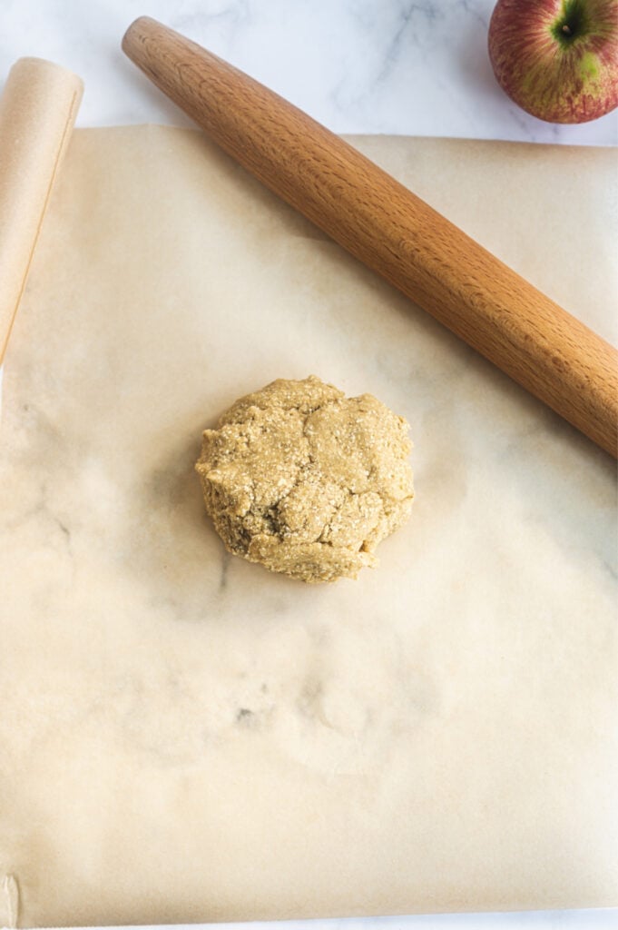 Overhead photo: brown parchment paper with a ball of Gluten Free dough and a wooden rolling pin