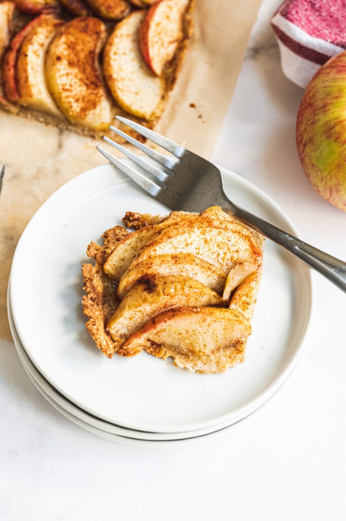 A piece of gluten free apple tart on a white plate with a fork on the side.