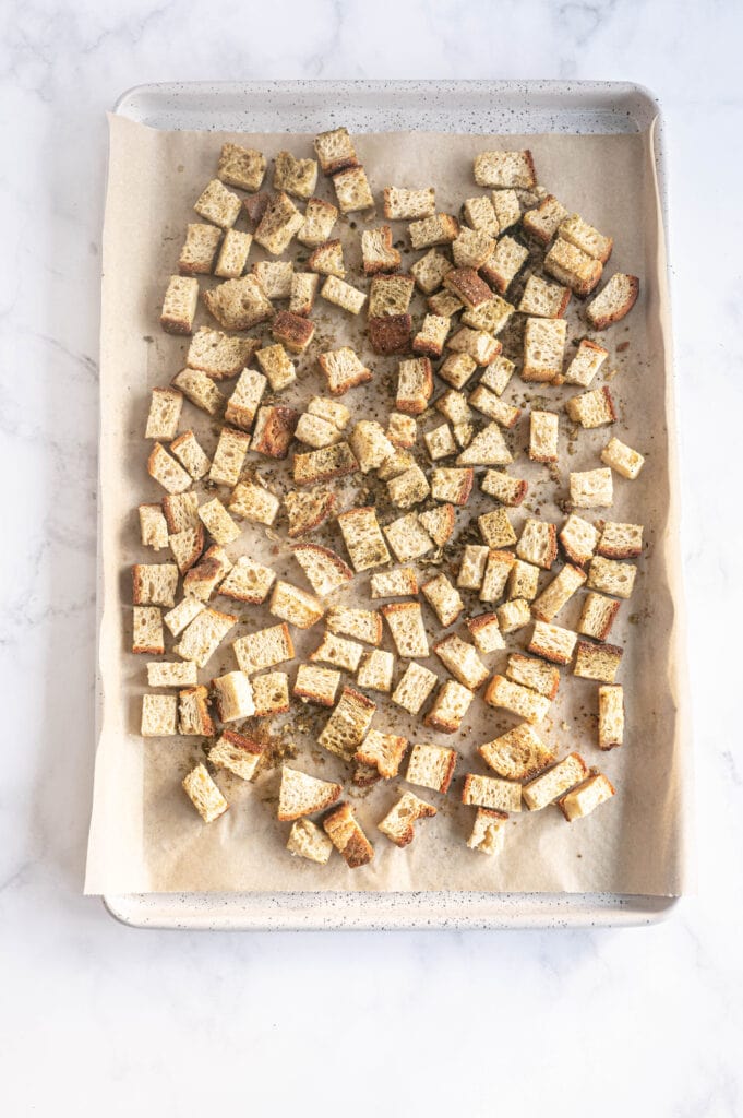 Bread cubes on a parchment lined baking sheet, ready to be toasted in the oven.