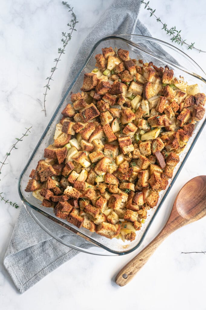 Glass baking dish filled with homemade bread stuffing with a wooden spoon on the side.