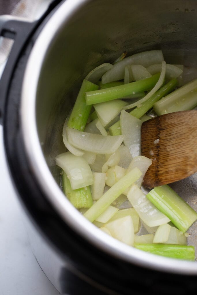 Onions and celery in an Instant Pot with a wooden spoon