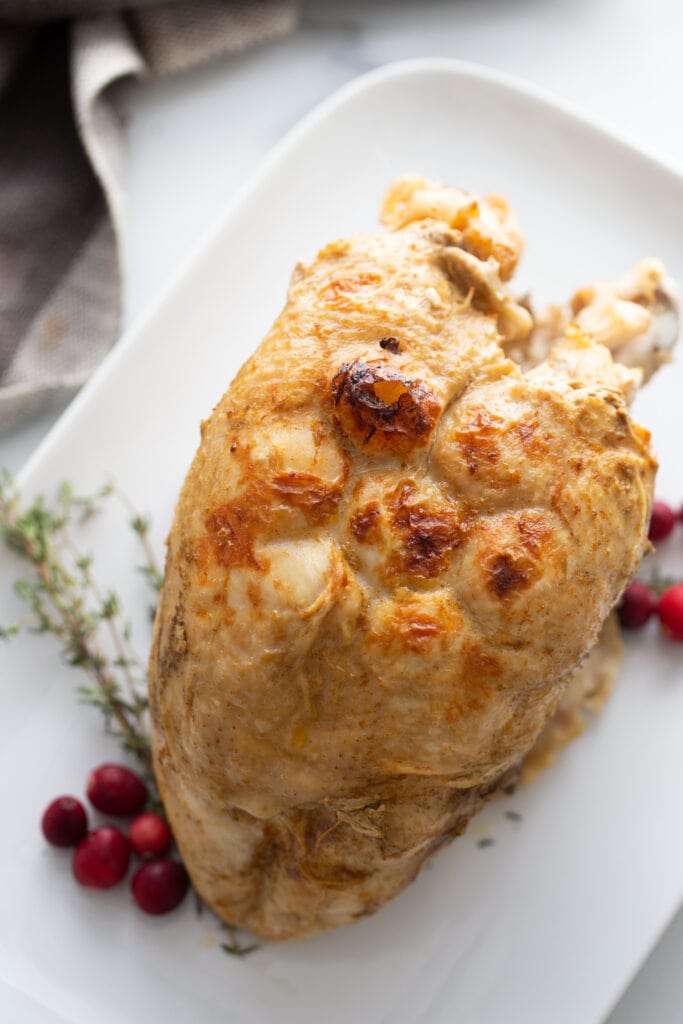 Instant pot turkey breast with crispy skin on a white serving dish. Cranberries and thyme are garnishes on the side.