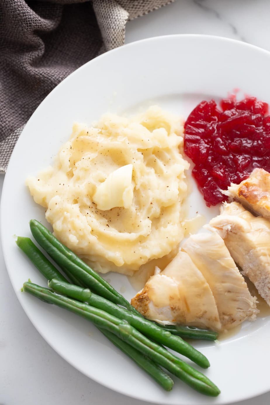 A plate of turkey breast, mashed potatoes, green beans, and cranberry sauce. 
