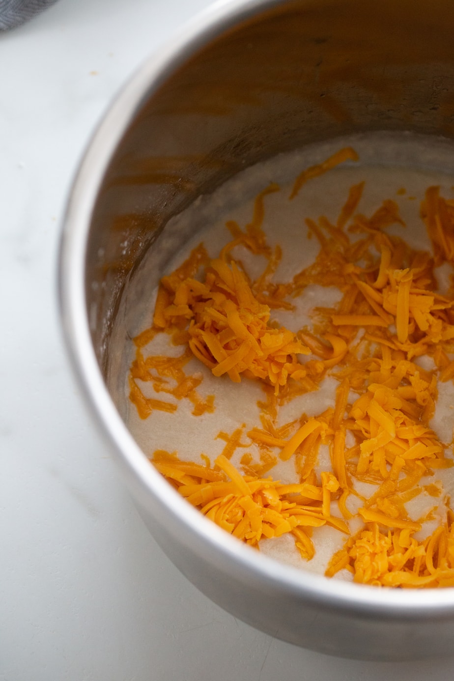Shredded yellow cheddar cheese is in a pot.