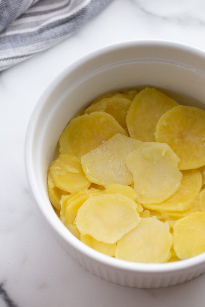 Sliced yellow potatoes are placed in a white mixing bowl.