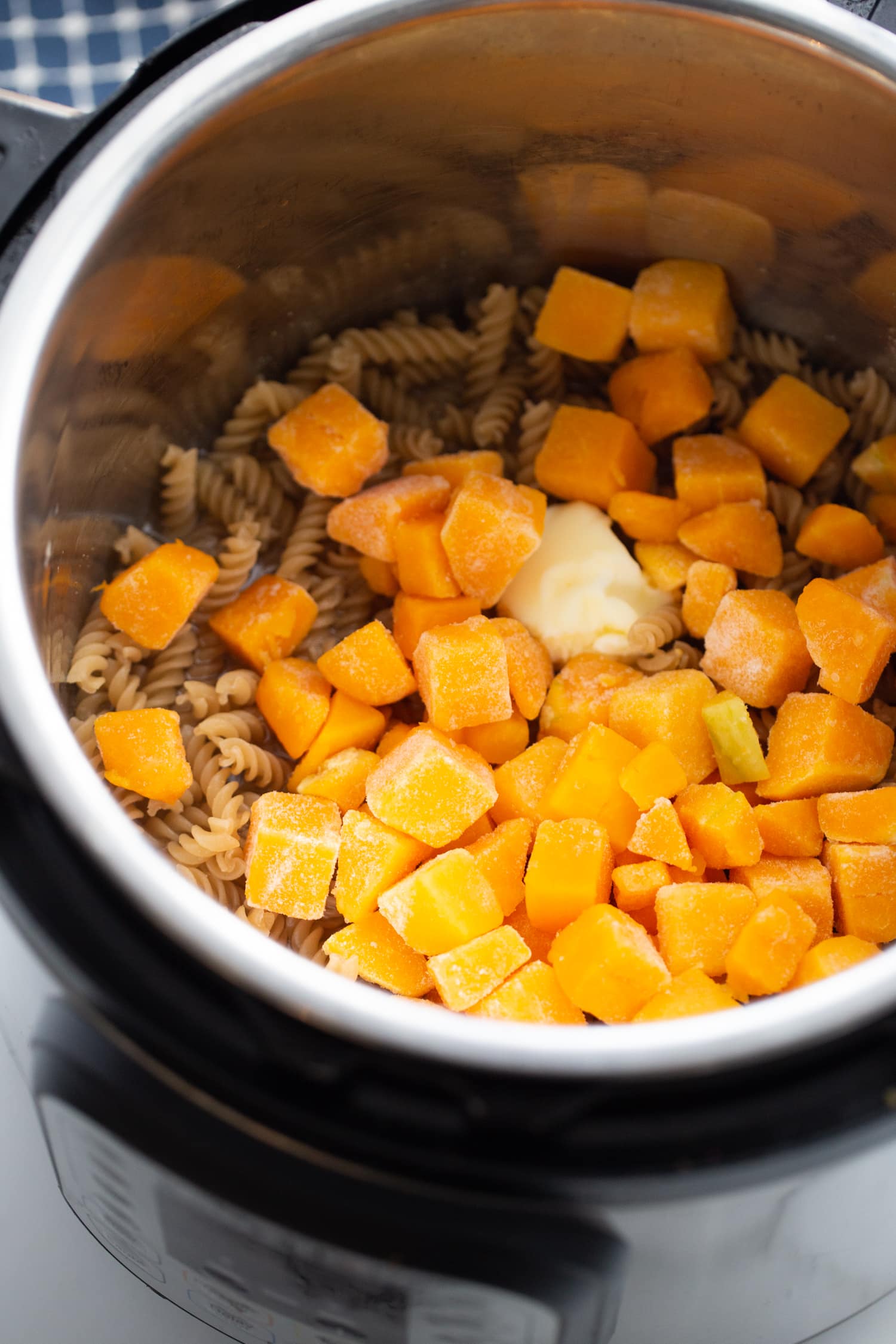 overhead photo of rotini pasta with cubed frozen butternut squash ready to be cooked in the instant pot.