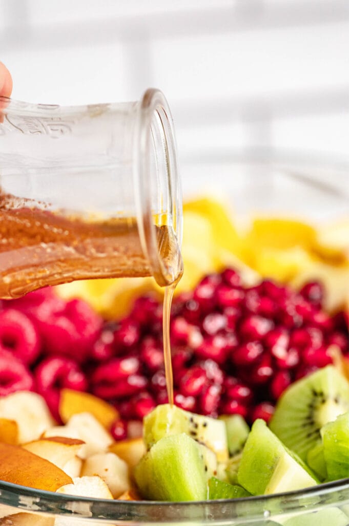 Maple syrup in a glass container is drizzled over pieces of green kiwi.