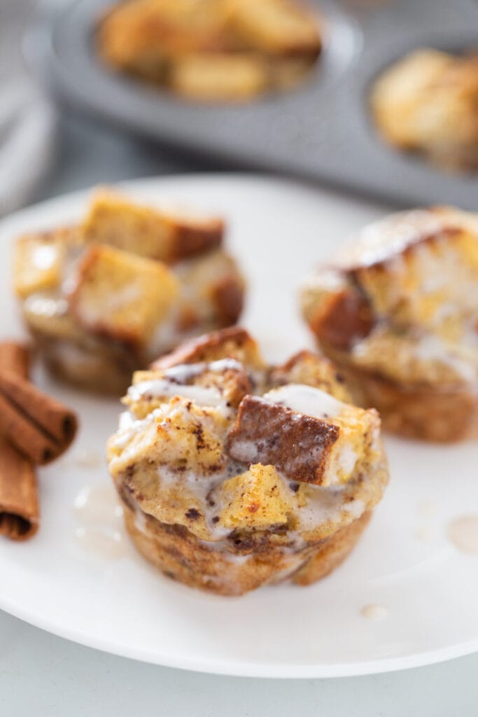 Cinnamon sticks are on a white plate of cinnamon French toast caasserole cups