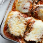 A glass baking dish holds freshly baked slices of eggplant parm.