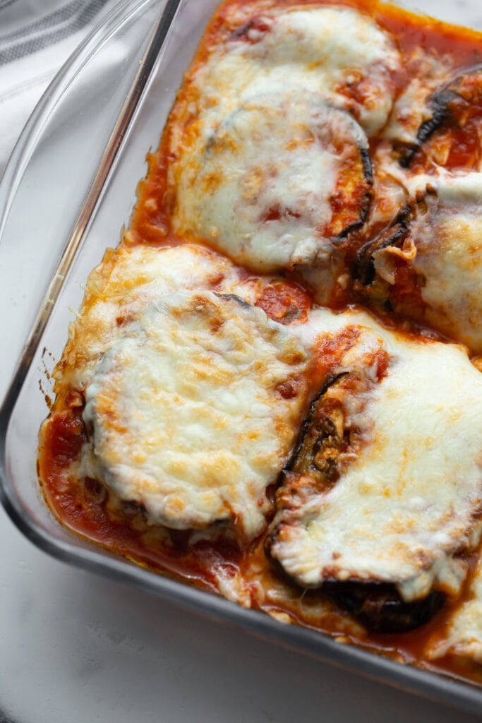 A glass baking dish holds freshly baked slices of eggplant parm.