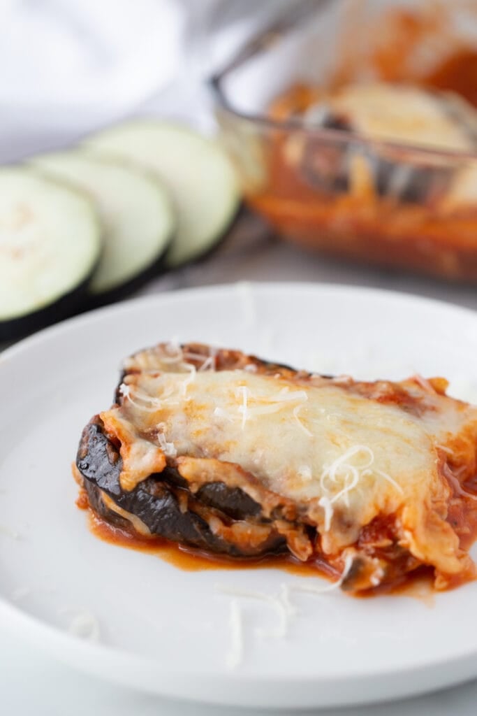 A portion of eggplant parm is placed on a white plate, ready to be eaten.