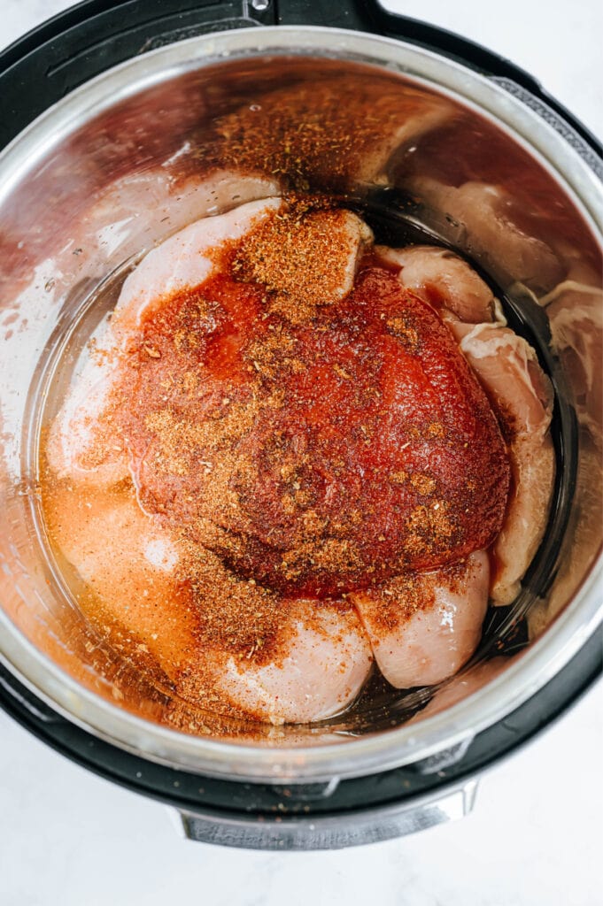 Raw chicken is in an Instant Pot with seasoning on it.