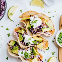 Three chicken tacos are garnished with cilantro and greek yogurt.