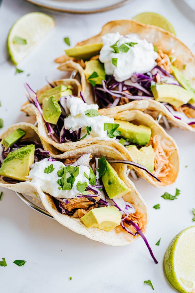 A close up shot reveals multiple fresh veggies garnishing three chicken tacos.
