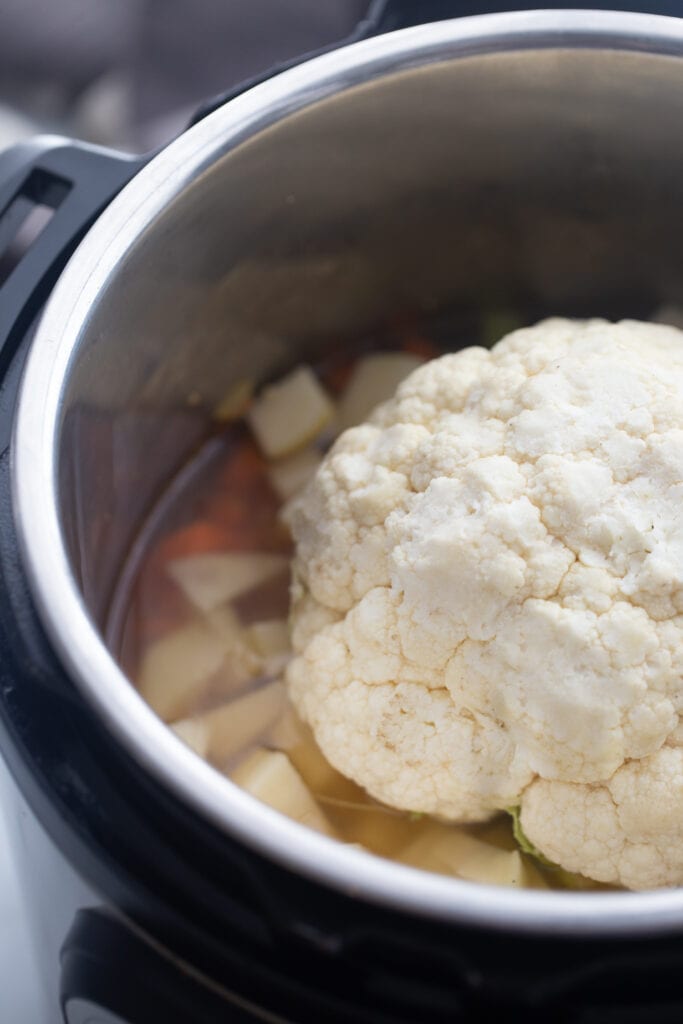A head of cauliflower sits on top of the other ingredients in the pot.
