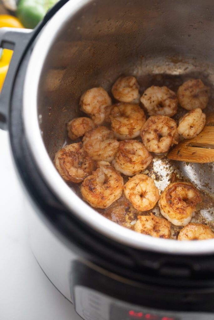 Cooked shrimp are being stirred with a wooden spoon in the Instant Pot.