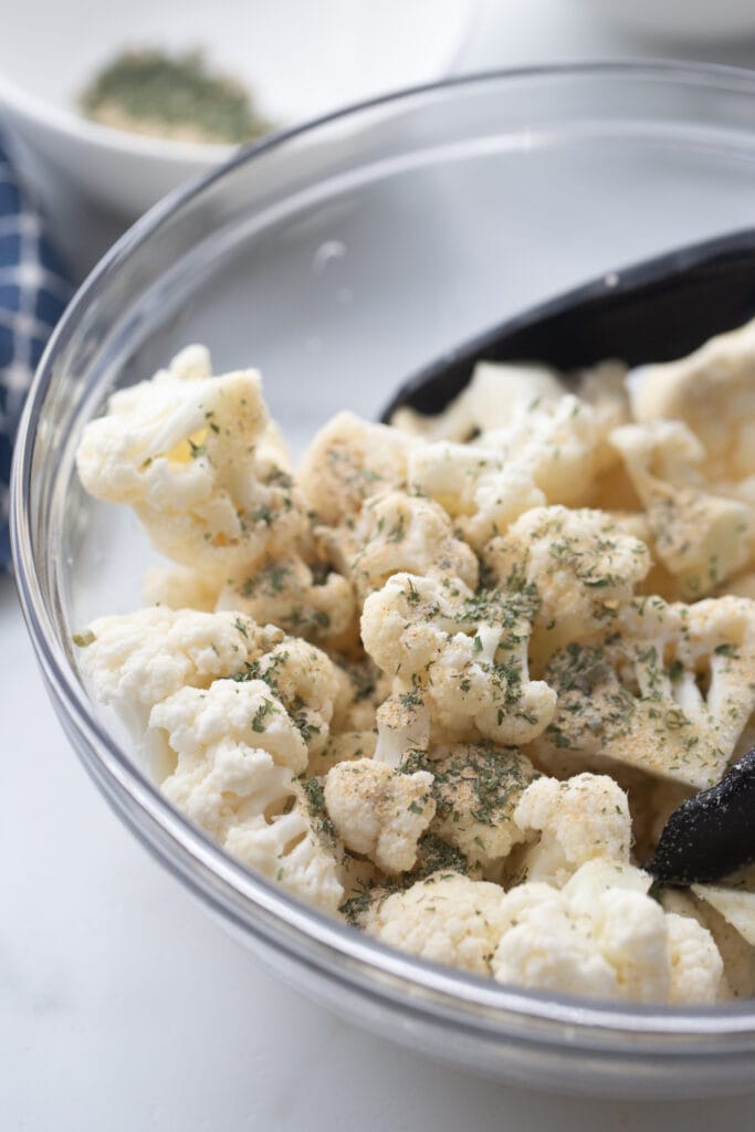 Cauliflower in a glass bowl tossed with homemade ranch seasoning, ready for the air fryer