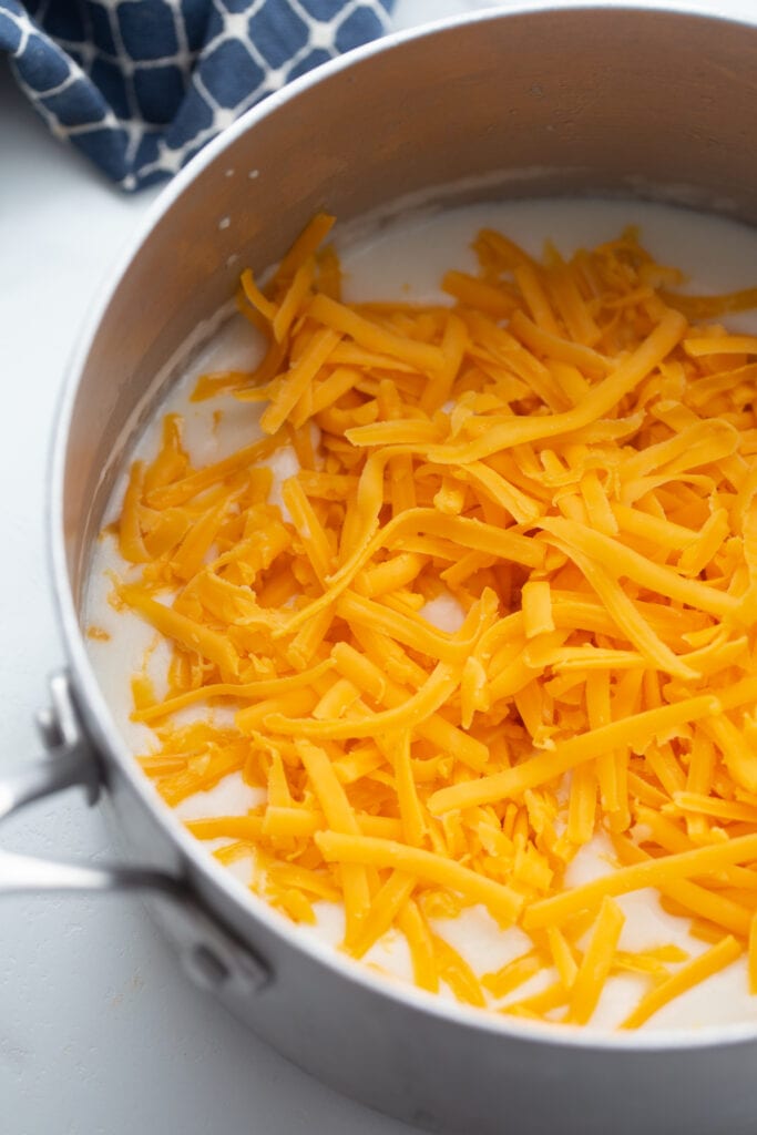 Overhead image: shredded cheddar cheese in a pot, ready to mix into homemade cheese sauce.