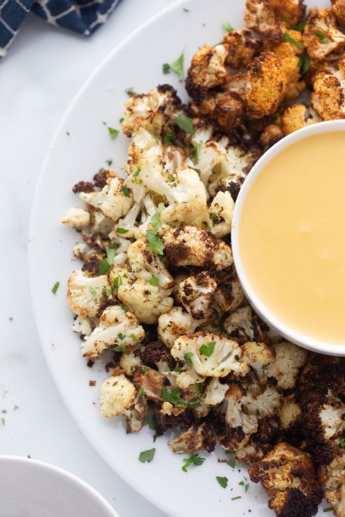 Overhead image: half of a large serving platter of air fryer cauliflower with healthy cheese sauce.