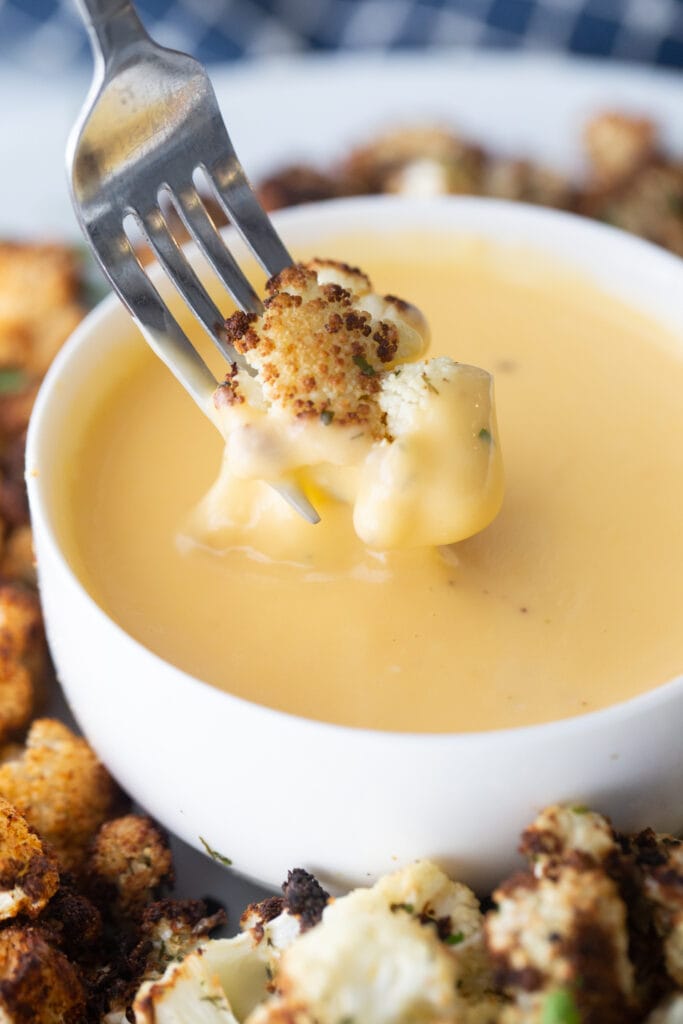Close up photo: fork dipping crispy air fryer cauliflower in a bowl of healthy cheese sauce