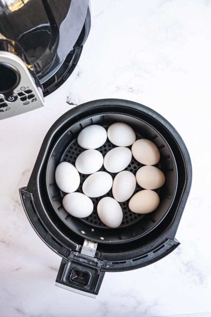 The air fryer basket is filled with a dozen uncooked eggs.