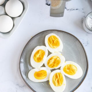 A plate of hard boiled eggs is placed next to raw eggs and an air fryer.