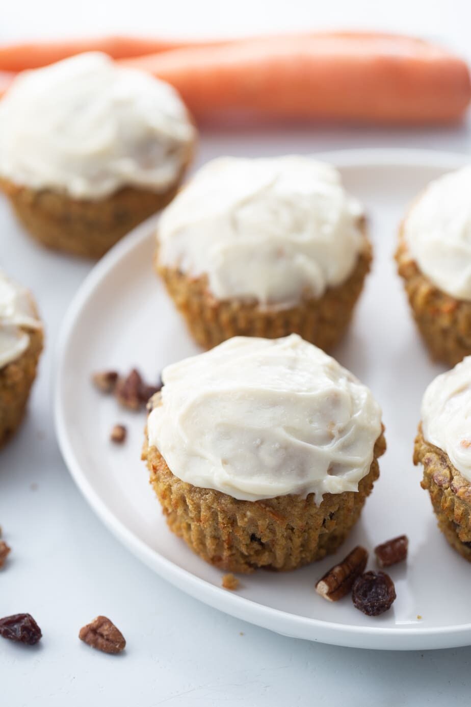 Six carrot cake muffins with frosting on a white plate