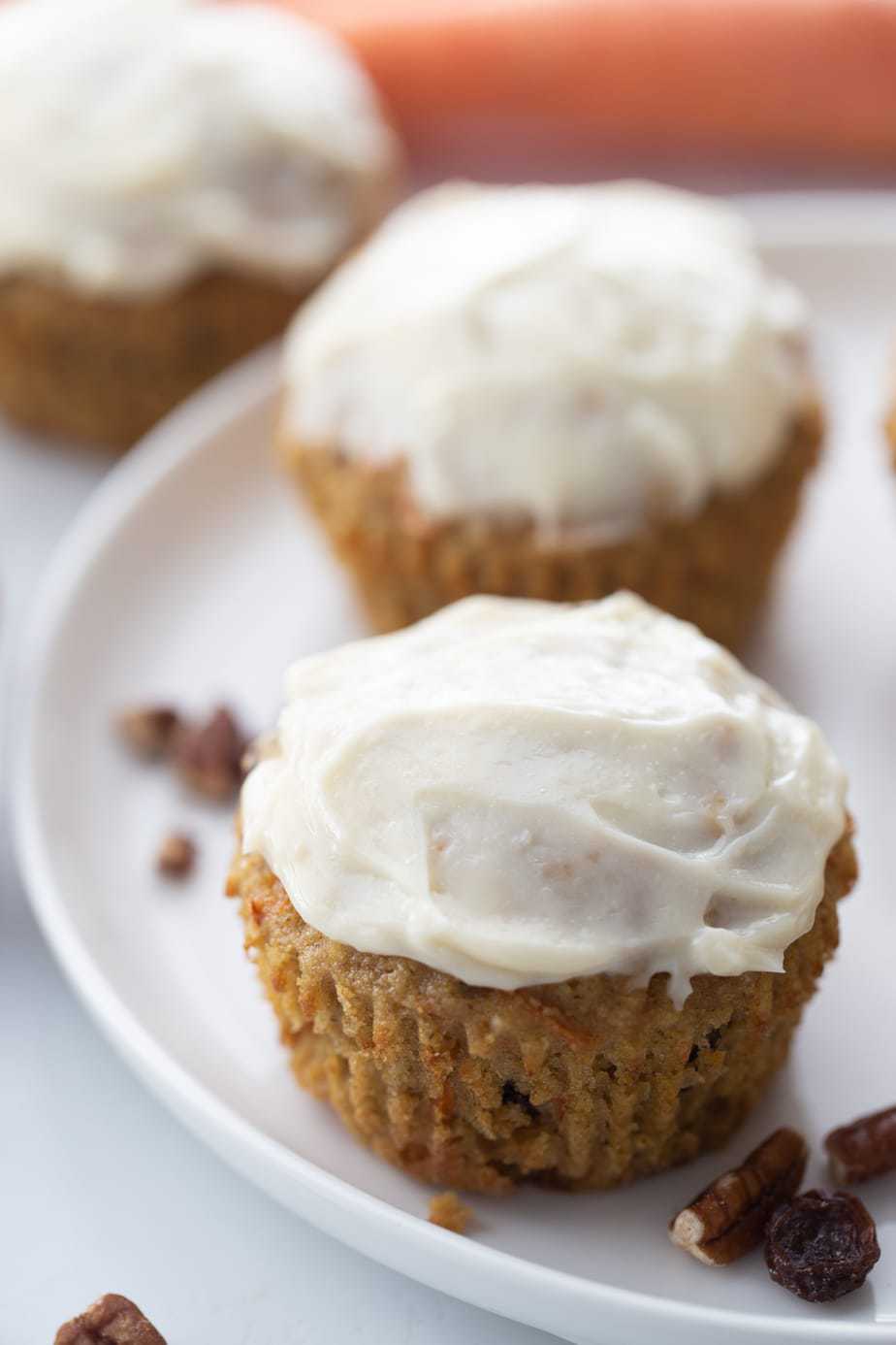 Two carrot cake muffins topped with cream cheese frosting on a white plate