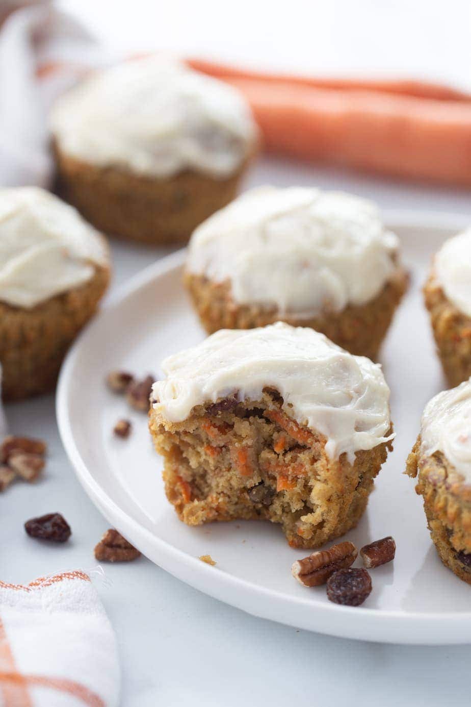 Carrot Cake muffins topped with cream cheese frosting on a white plate. Some cakes are in the background off of the serving plate.