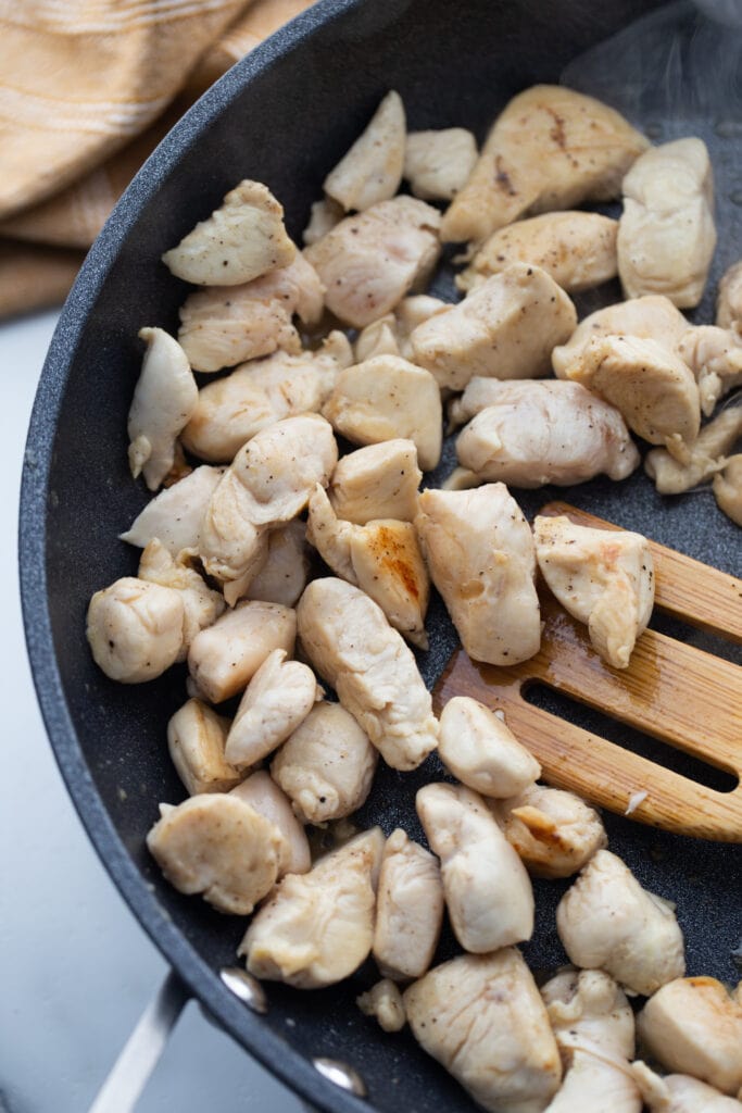 Diced chicken is being cooked in a large skillet.