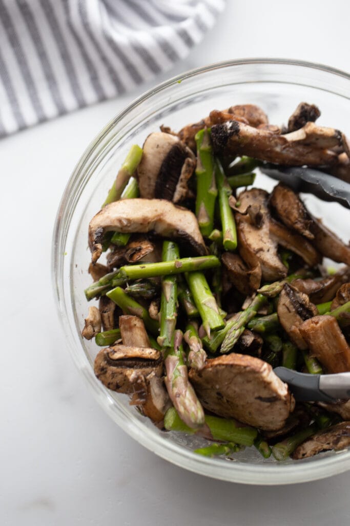 Asparagus and mushrooms are mixed in a glass bowl.