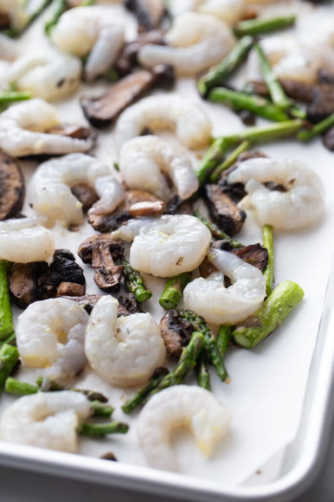 Shrimp and veggies are spread out on a baking sheet.