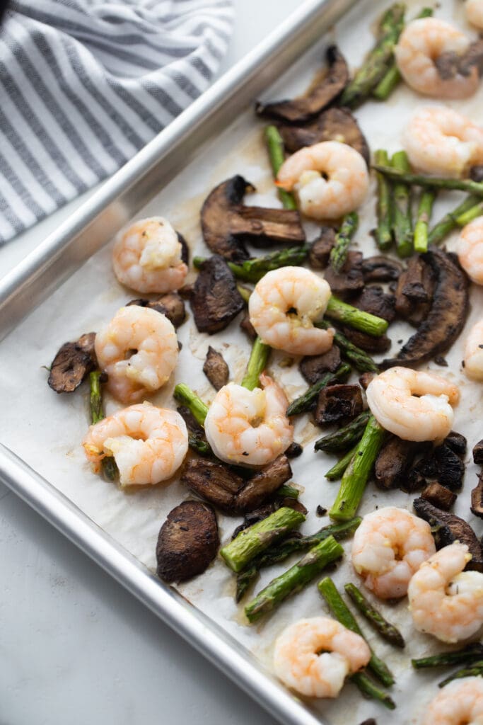 Baked shrimp and veggies are on a baking sheet.