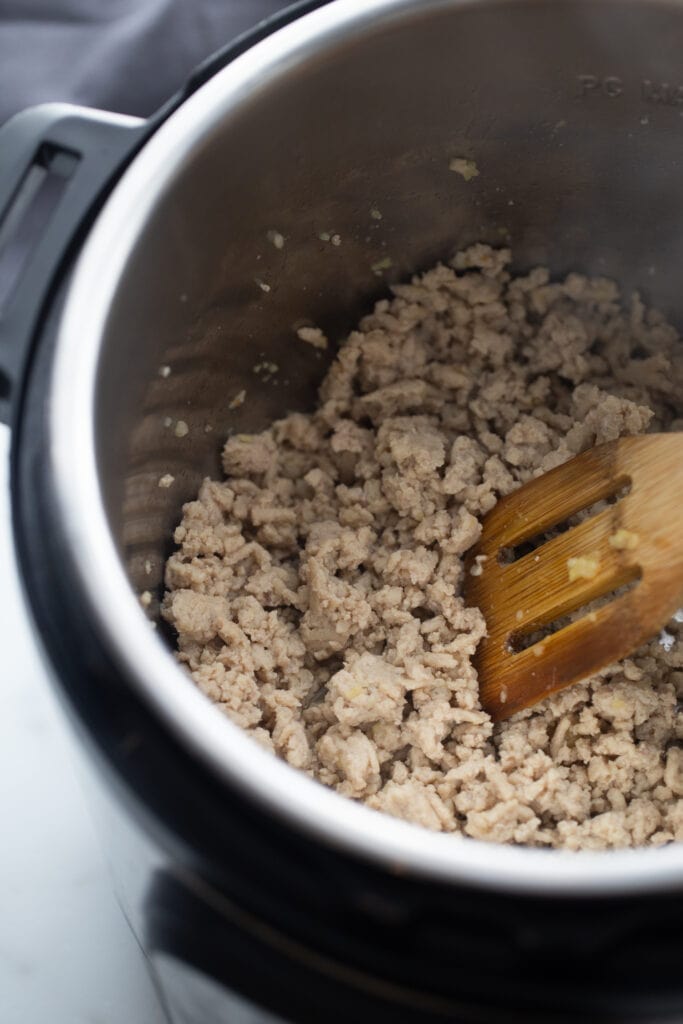 Overhead photo of cooked ground chicken in the Instant Pot with a wooden slotted spoon.