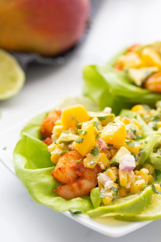 A plate of shrimp tacos with corn, mango, and avocado on top