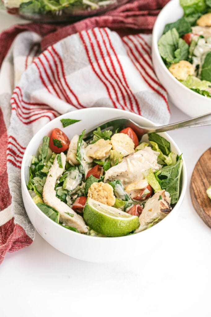 High angle photo of an individual serving of Caesar salad in a white bowl.