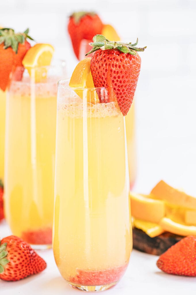 Champagne flutes with orange strawberry mimosas and a strawberry garnish 