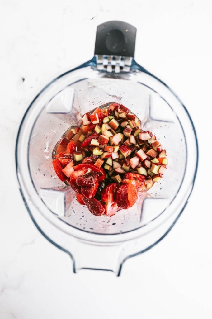 An overhead shot of a blender with frozen strawberries, rhubarb, and liquid 
