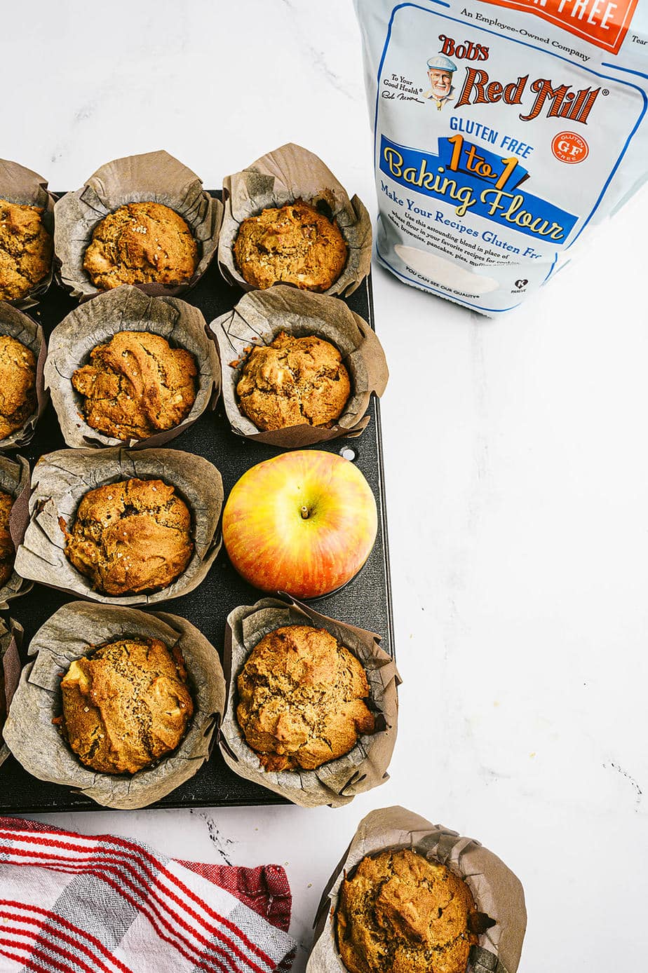 Apple muffins on a white marble table next to a bag of gluten free flour. 