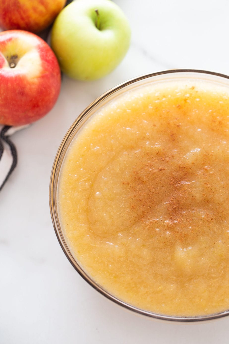 A clear bowl of applesauce with apples in the upper left hand corner 