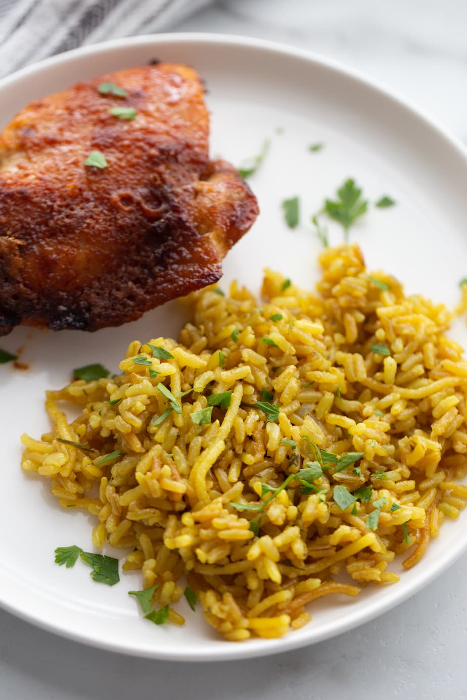 A white plate with homemade rice a roni and Air Fryer chicken thighs garnished with fresh parsley. 