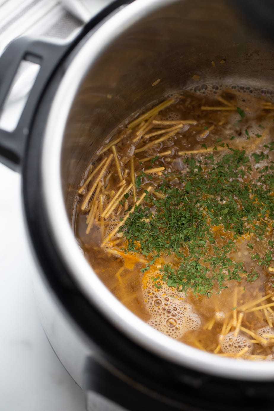 In process shot of instant pot rice a roni - rice, spaghetti, and herbs in a pot. 