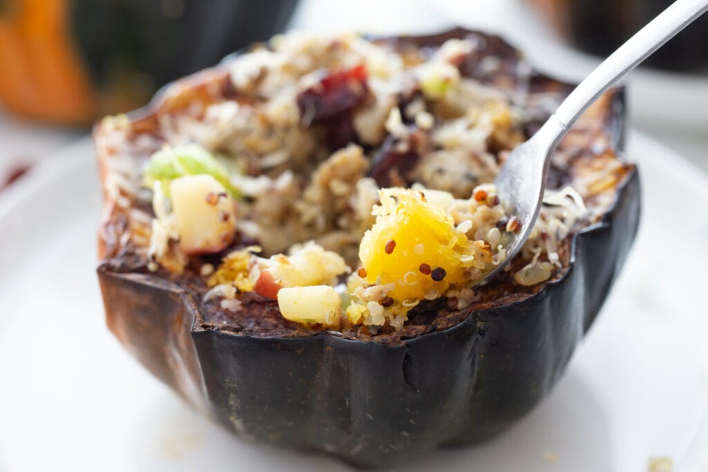 Close up photo of a fork digging into acorn squash stuffed with fall flavors.