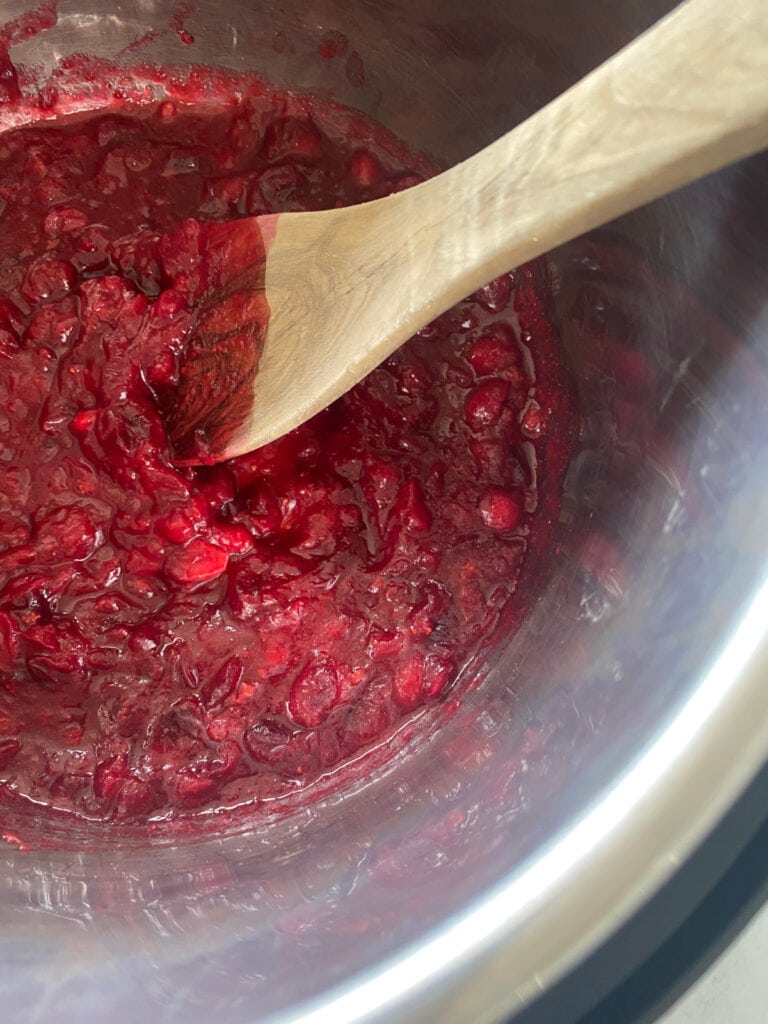 Cooked cranberry sauce in an Instant Pot liner with a wooden spoon.
