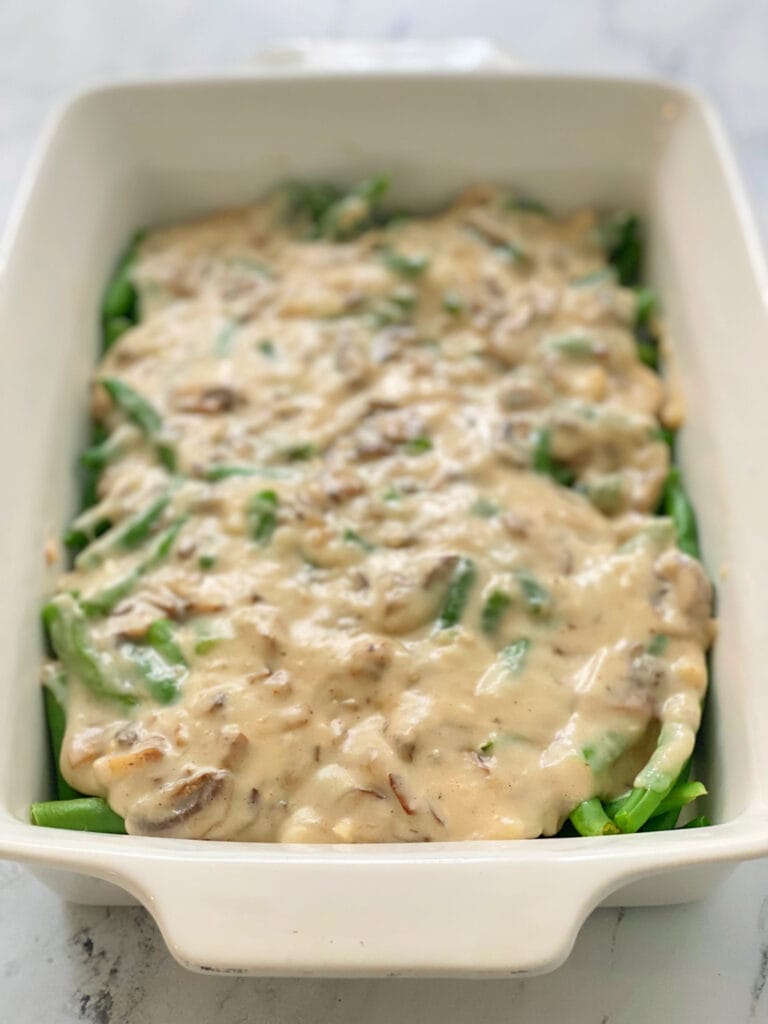 High angle view: fresh green beans topped with homemade mushroom alfredo sauce in a casserole dish.