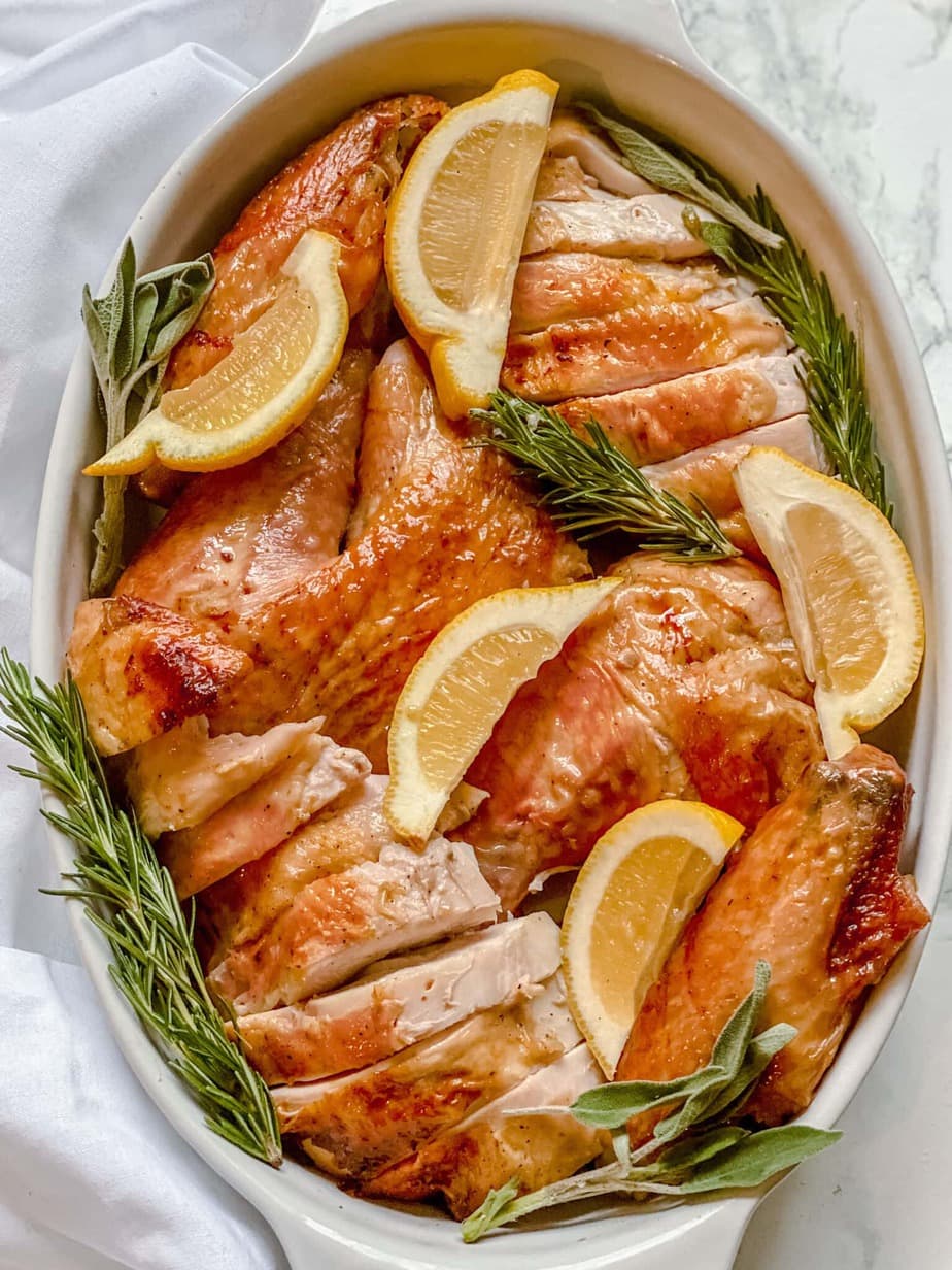 Overhead image: sliced whole turkey in a white baking dish with lemon slices and sprigs of rosemary